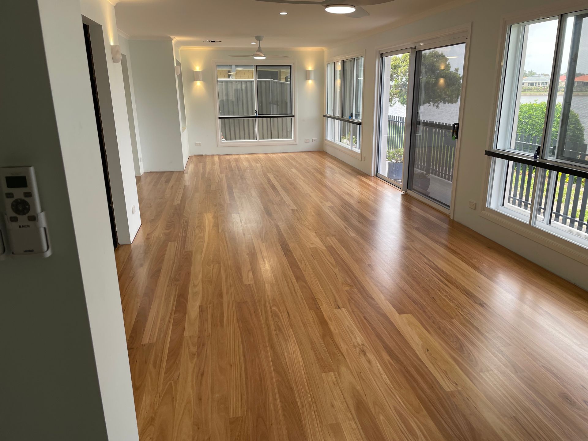 An Empty Living Room With Hardwood Floors and Lots of Windows — Scott Graham Building Services In Bilambil Heights, NSW
