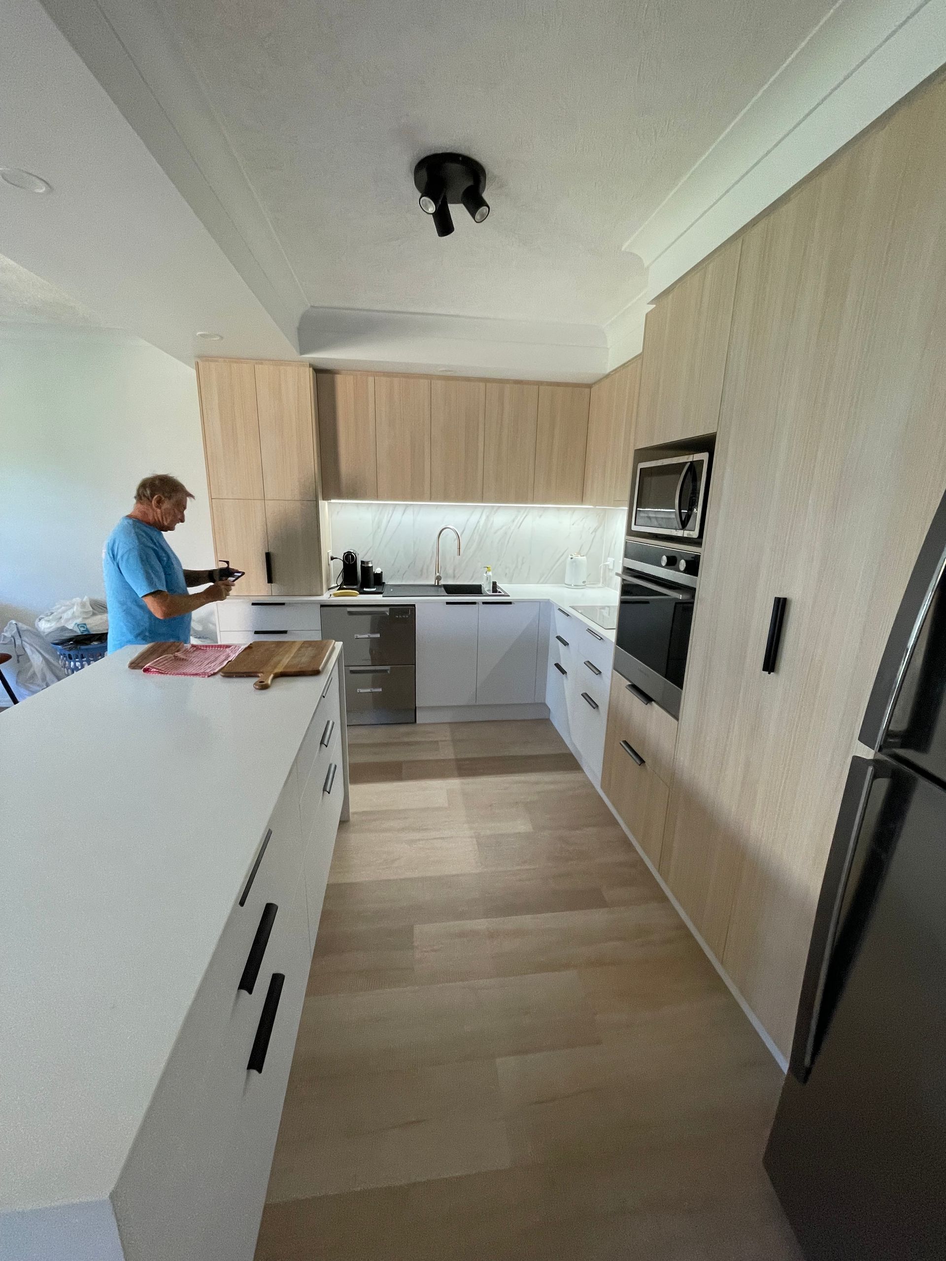 A Man is Standing in a Kitchen Looking at a Tablet — Scott Graham Building Services In Bilambil Heights, NSW