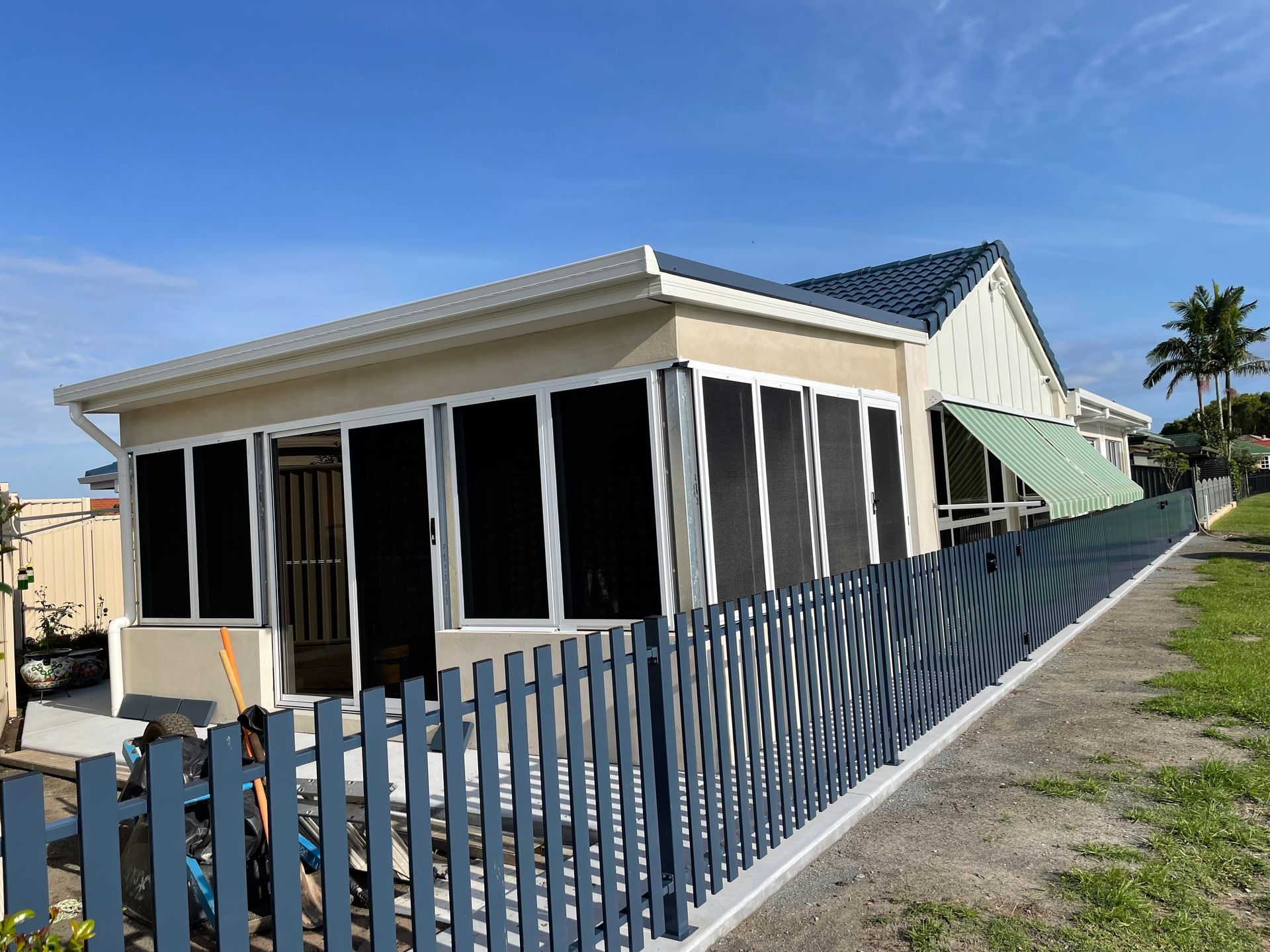A Small House With a Blue Fence Around It — Scott Graham Building Services In Bilambil Heights, NSW