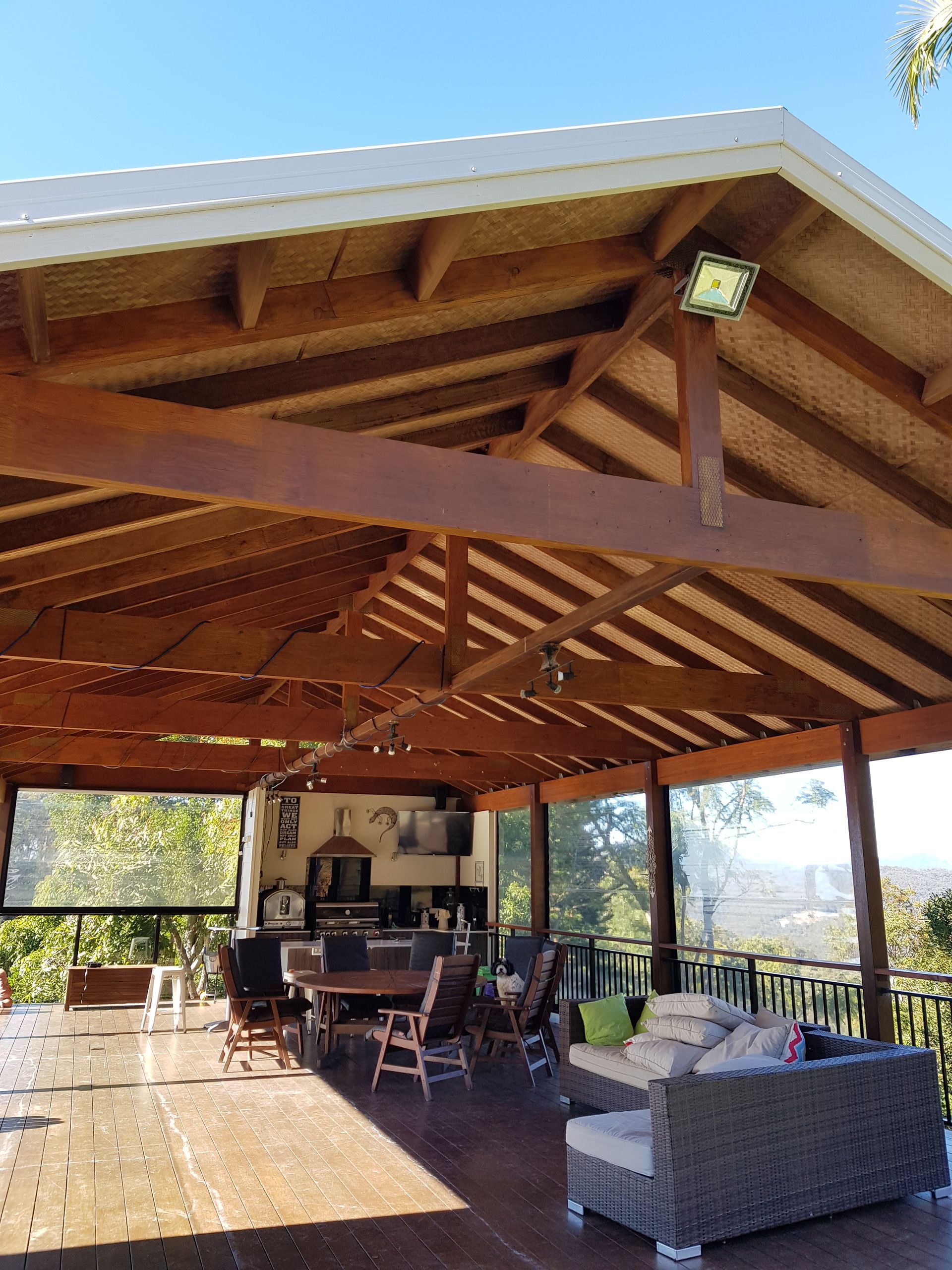 A Large Covered Patio With a Table and Chairs Under a Wooden Roof  — Scott Graham Building Services In Bilambil Heights, NSW 