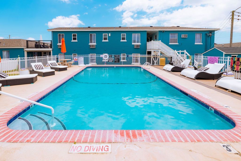 An inviting outdoor pool area at Seabirds Motel at Kure Beach with lounge chairs, umbrellas, and clear blue water under a sunny sky. This space provides a refreshing retreat for guests, enhancing the pet-friendly lodging experience in North Carolina.