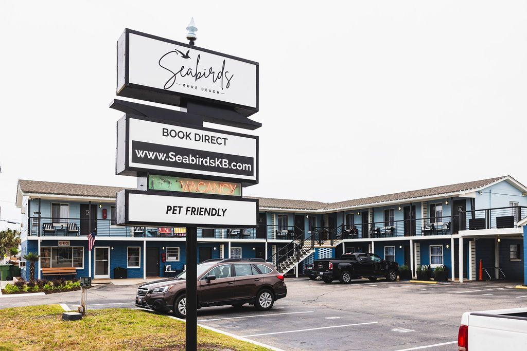 The exterior of Seabirds Motel at Kure Beach, featuring a welcoming sign and ample parking space. The motel's modern facade highlights its pet-friendly accommodations, offering a comfortable stay in North Carolina.
