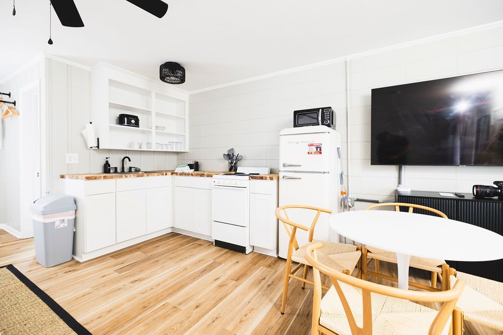 A stylish kitchenette at Seabirds Motel at Kure Beach, equipped with a microwave, refrigerator, sink, and a flat-screen TV. The dining table and chairs provide a functional space for meals, ideal for guests enjoying a pet-friendly stay in North Carolina.