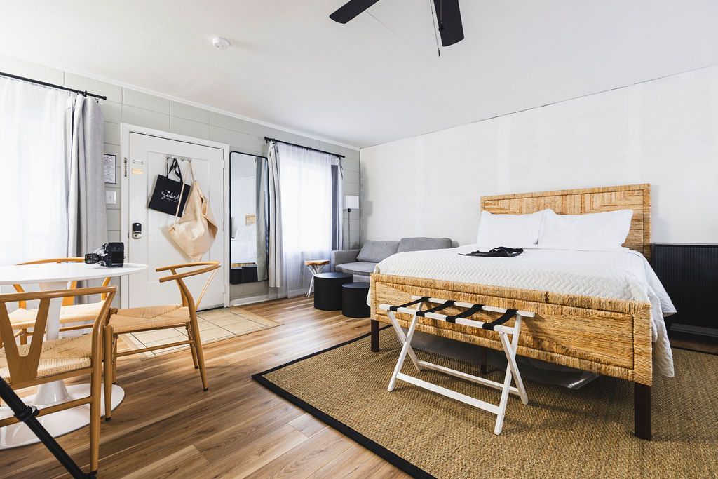 A cozy guest room at Seabirds Motel at Kure Beach featuring a queen-sized bed with a rattan frame, a small dining area, and a seating area with a sofa. The room's design provides a comfortable and flexible space, perfect for a pet-friendly lodging experience in North Carolina.