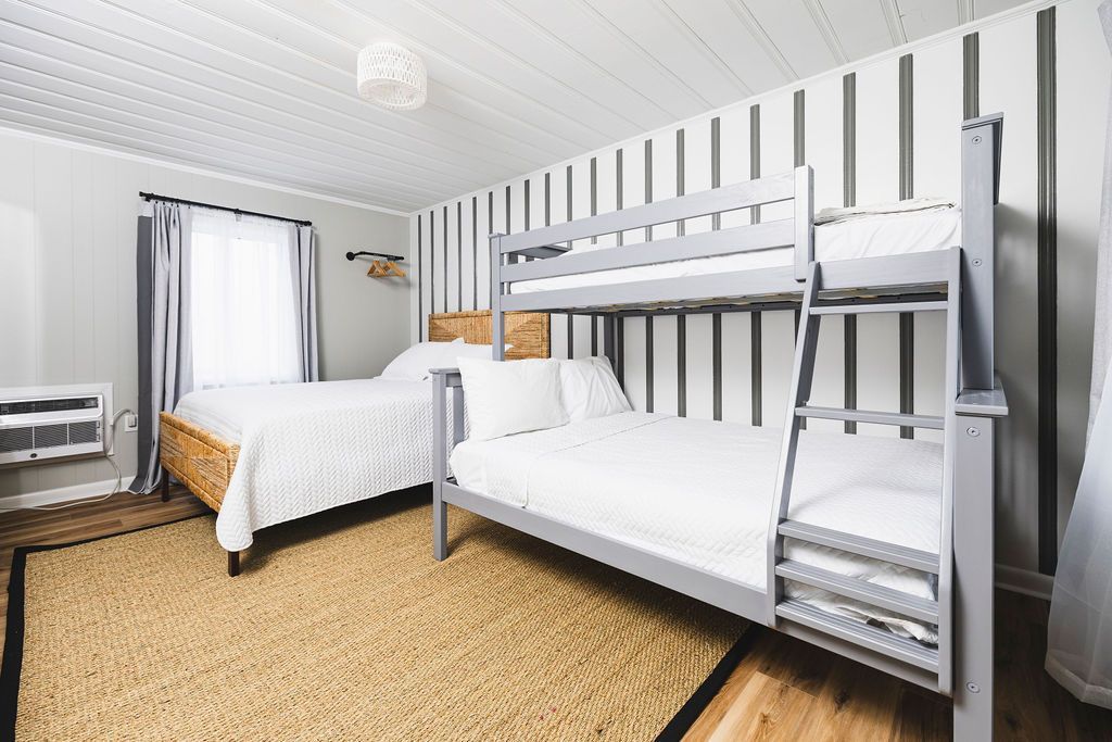 A bright family-friendly room at Seabirds Motel at Kure Beach featuring a queen-sized bed with a rattan frame and a set of bunk beds, offering versatile sleeping arrangements for families or groups. The room's coastal decor provides a welcoming, pet-friendly North Carolina lodging experience.