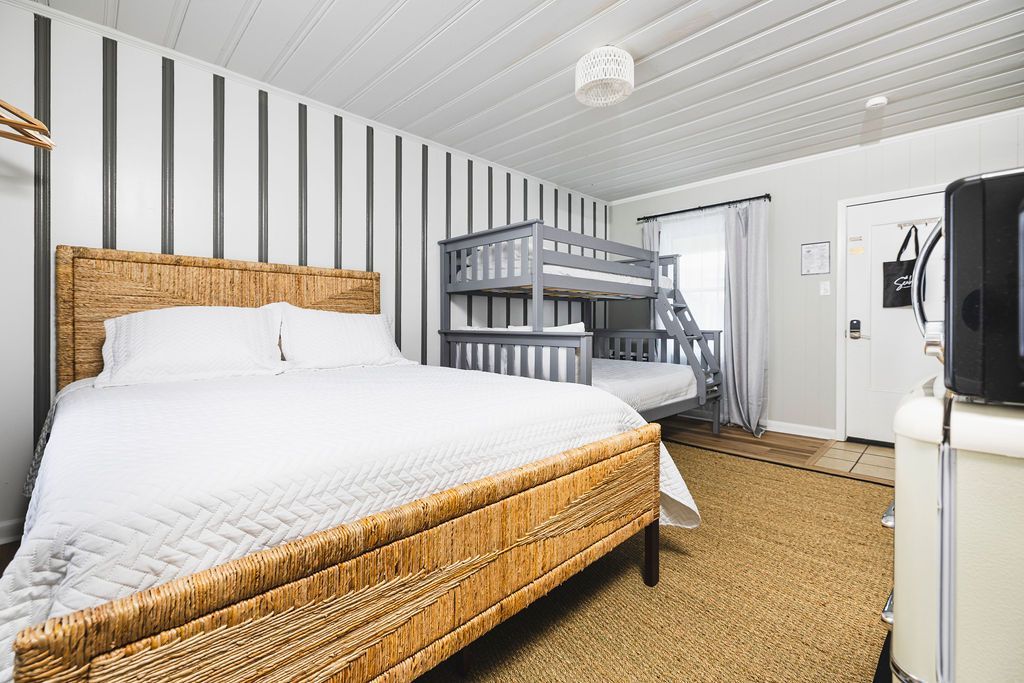 A spacious guest room at Seabirds Motel at Kure Beach with a queen bed, a bunk bed, and a mix of rattan and contemporary furniture. This room is designed for comfort and functionality, ideal for families and guests traveling with pets, offering a relaxed stay at this pet-friendly North Carolina lodging.