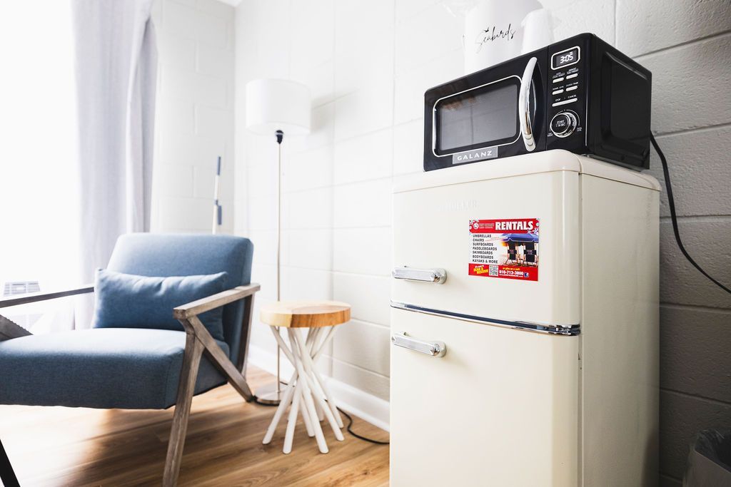 A corner of a guest room at Seabirds Motel at Kure Beach, featuring a retro-style mini-fridge and microwave, along with a comfortable blue chair and side table. The setup is perfect for enjoying a snack or drink, providing a convenient and pet-friendly lodging experience in North Carolina.