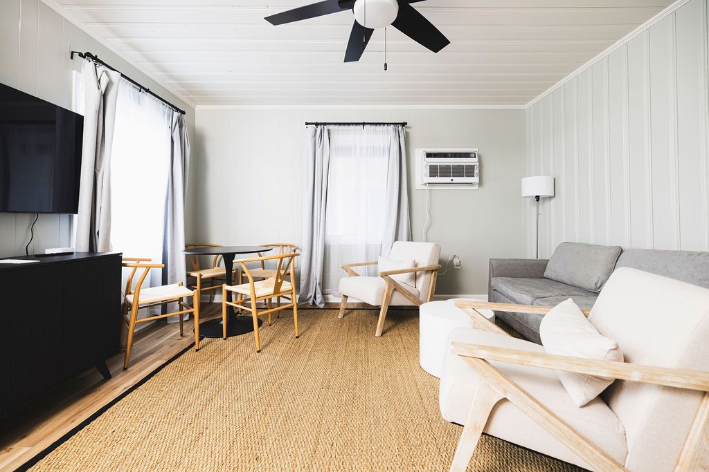 A spacious living room at Seabirds Motel at Kure Beach with a comfortable seating area, including a gray sofa and chairs, and a flat-screen TV. The room's open layout and natural light create a relaxing environment, perfect for a pet-friendly stay in North Carolina.