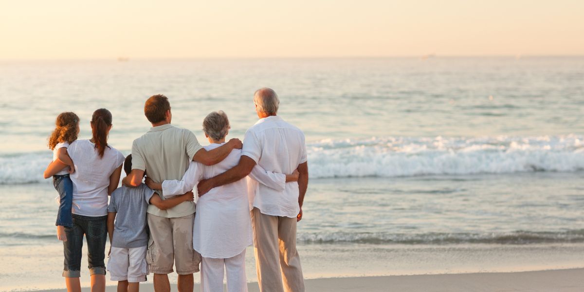 A multigenerational family standing together on Kure Beach, looking out at the ocean during sunset, creating a warm and memorable family moment.