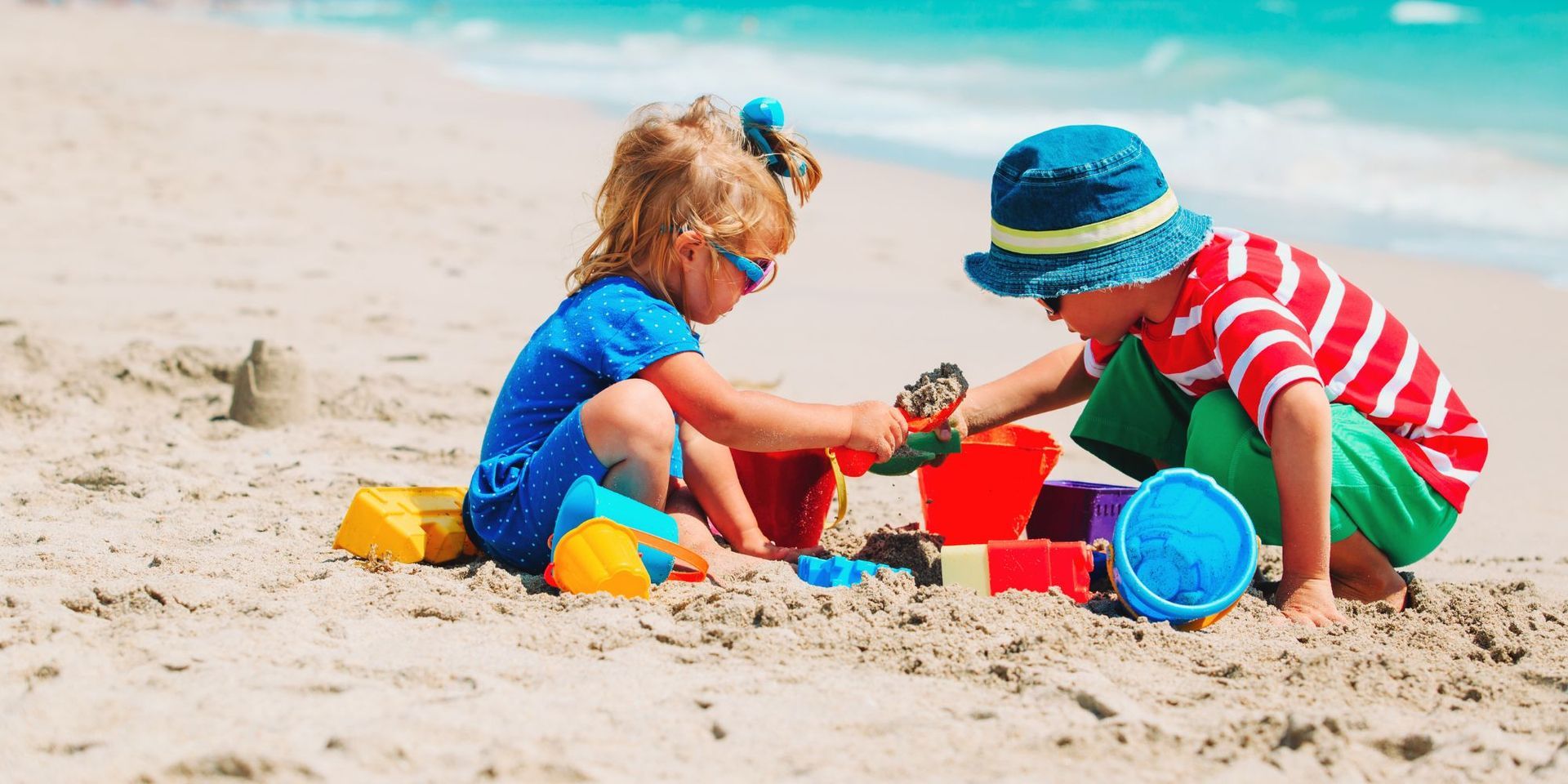 Two young children building sandcastles on the sandy shores of Kure Beach, with bright beach toys an