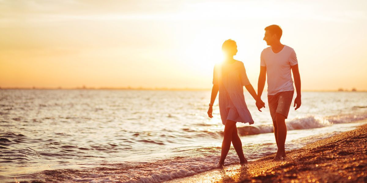 A couple holding hands while walking along Kure Beach at sunset, enjoying the warm glow and peaceful shoreline.