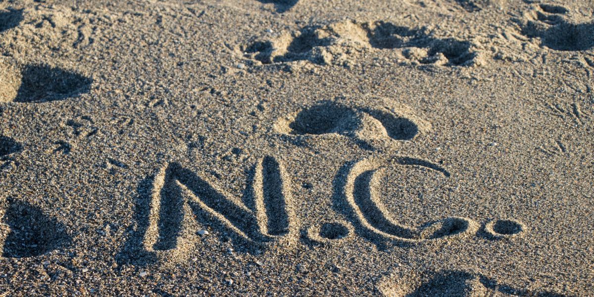 N.C.’ drawn in the sand on a North Carolina beach, capturing a simple, heartfelt tribute to the state’s beautiful coastline.