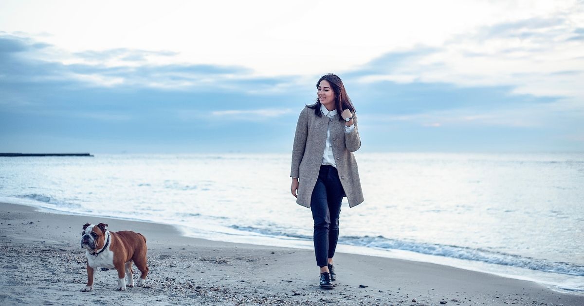 A young woman walking her dog along the peaceful shoreline of Kure Beach, enjoying the quiet charm of a winter day.