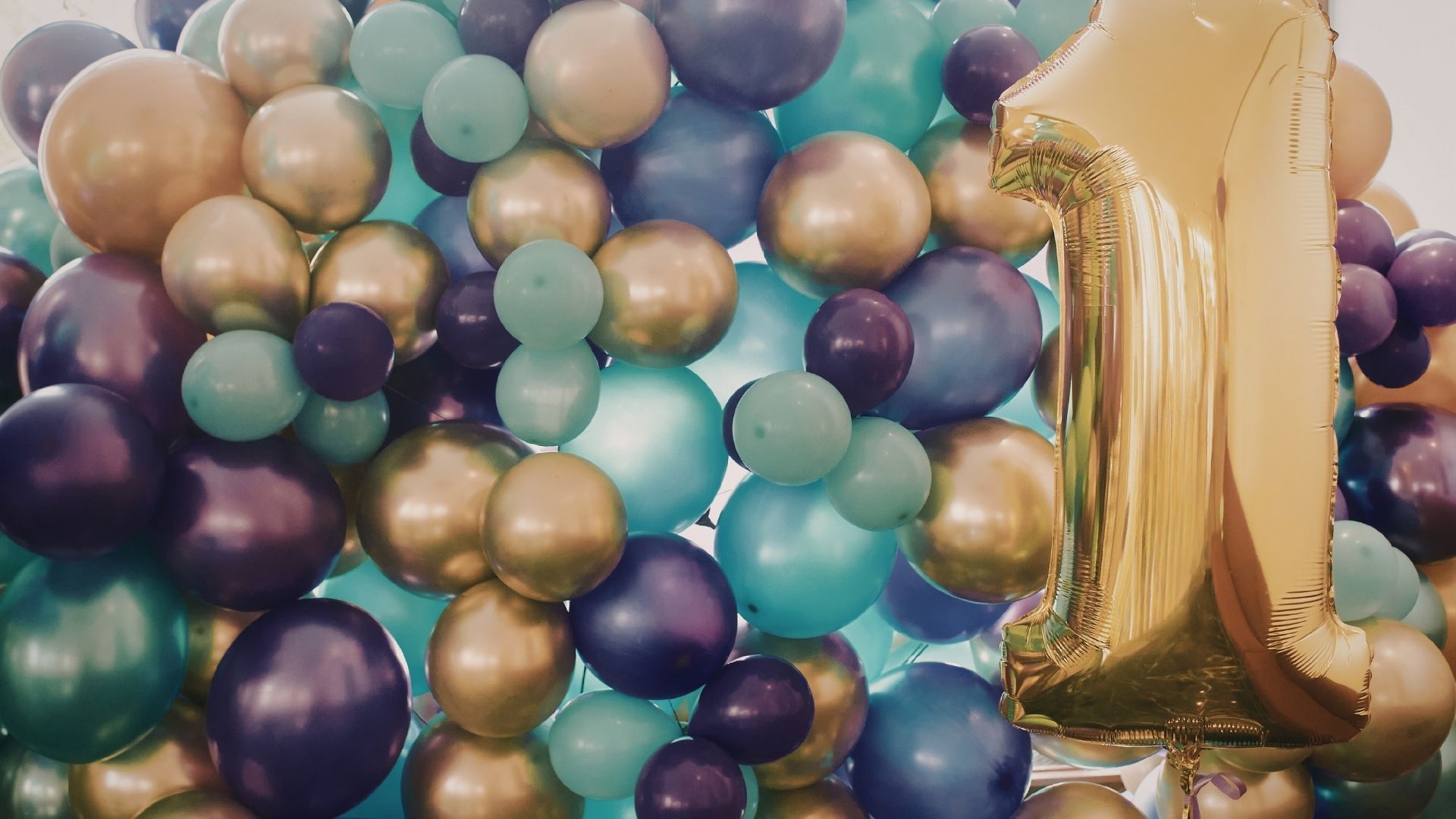 Gold foil balloon amid a cluster of teal, purple, and gold balloons