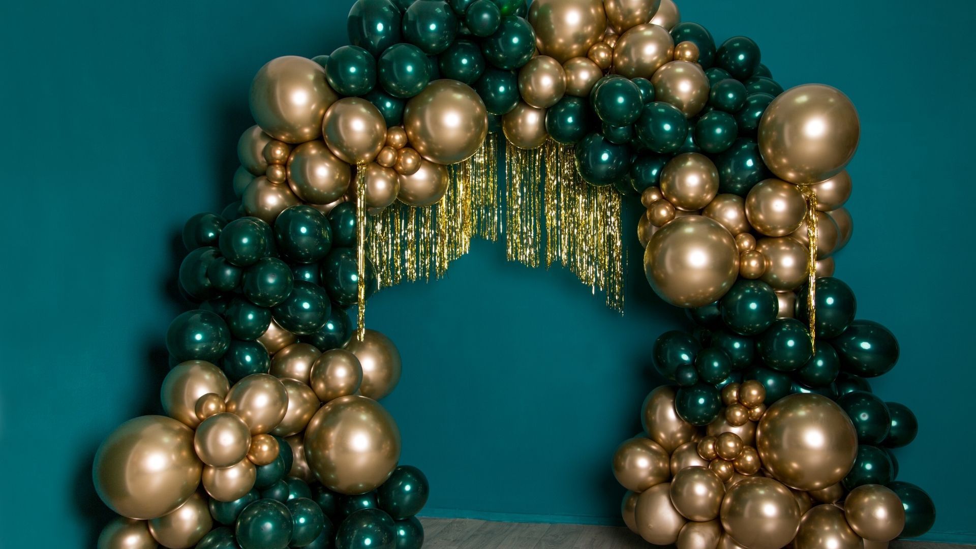 Balloon arch in teal, gold, and cream against a teal background