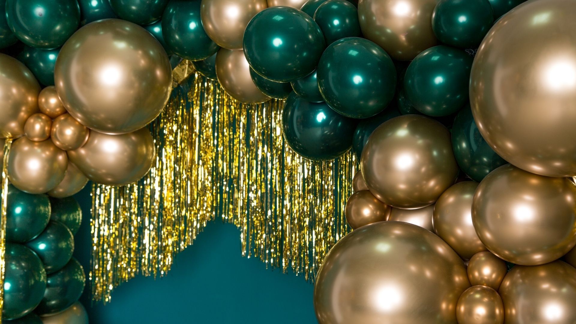 Teal and gold balloon arch with gold fringe backdrop, creating a festive party entrance