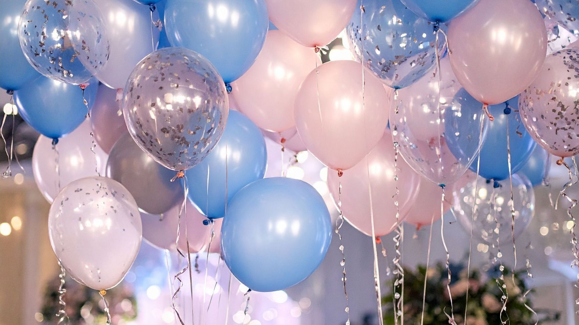 Pastel blue, pink, and silver balloons with confetti at an indoor celebration