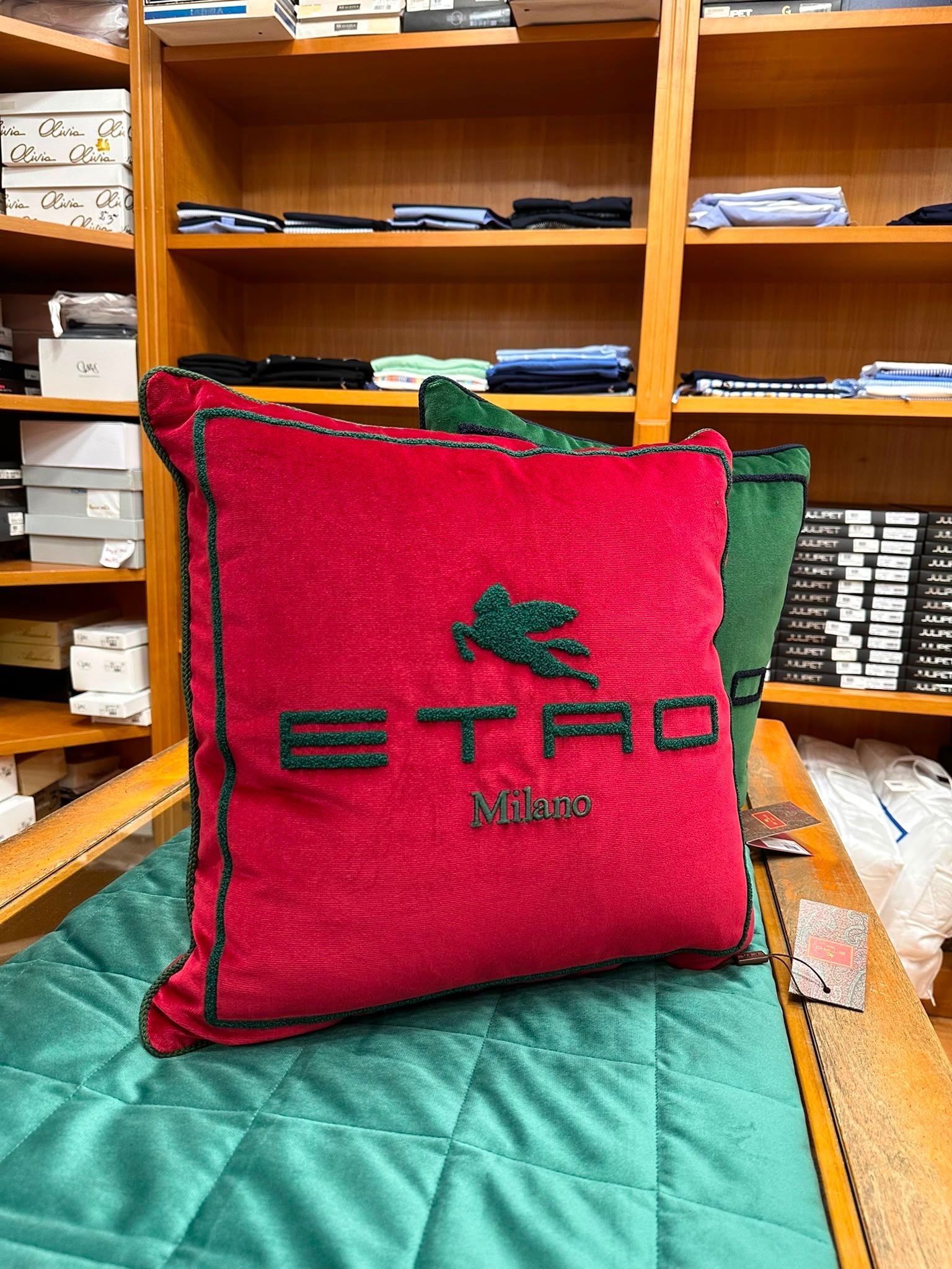 Cuscino rosso con il logo ETP su un copriletto trapuntato verde, con mensole in legno sullo sfondo.