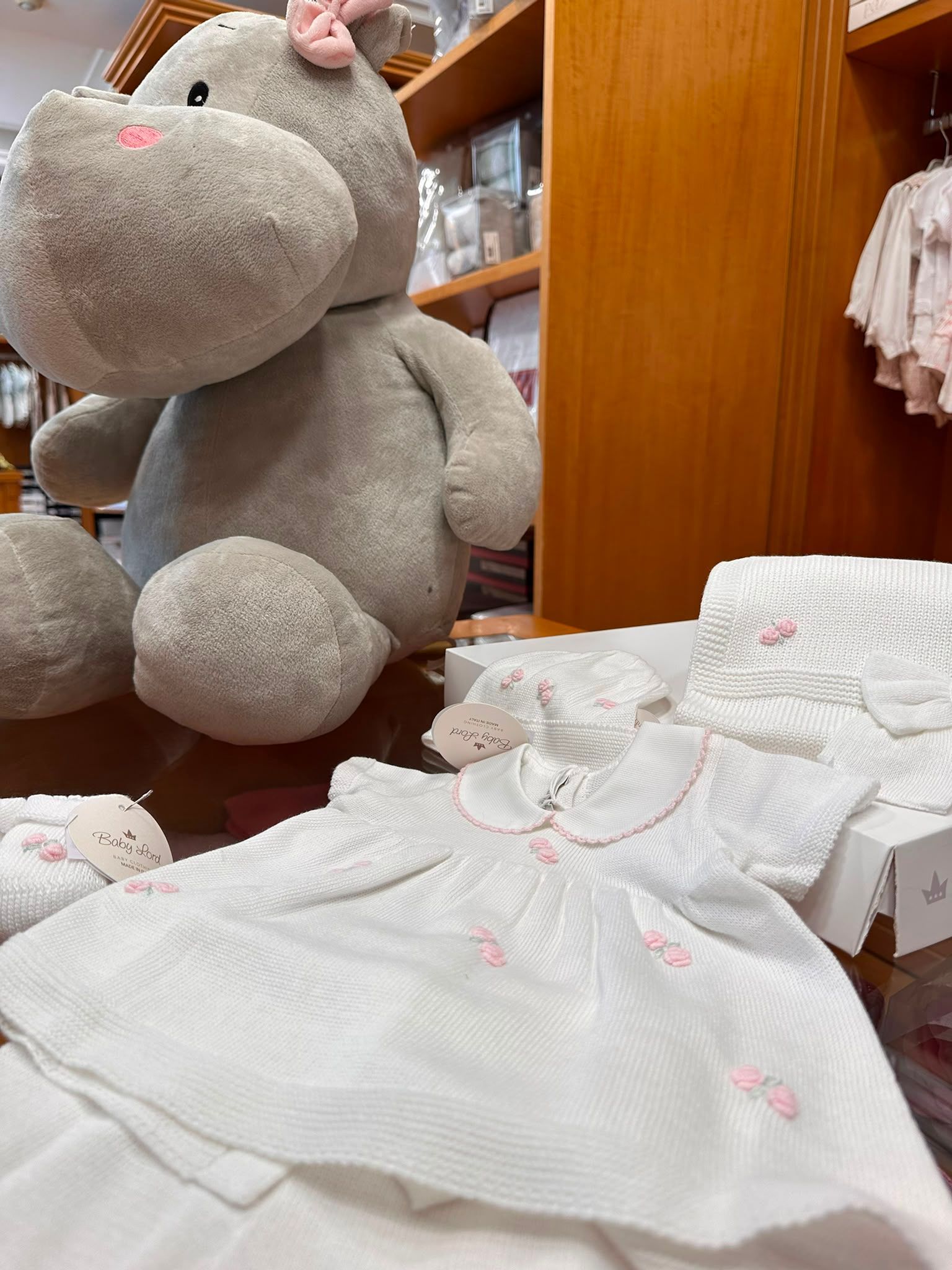 Vestitini bianchi da bambina esposti accanto a un grande ippopotamo grigio imbalsamato in un negozio