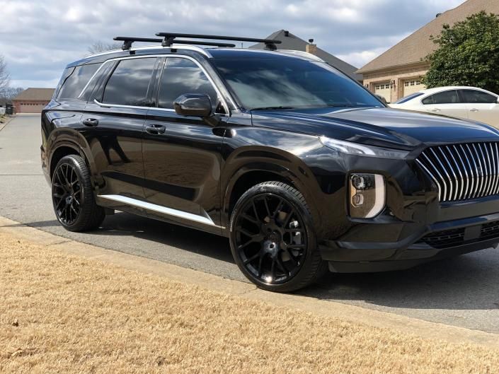 Black SUV parked by a curb on a sunny street, with roof cargo and black wheels