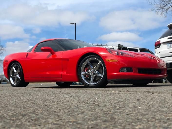 Red sports car parked on pavement under a blue sky, low-angle view