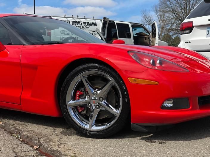 Red sports car parked outdoors, front-left view, with chrome wheels and a cracked asphalt lot background