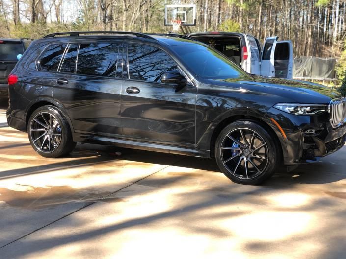Black SUV parked on a driveway, with trees and a basketball hoop in the background.