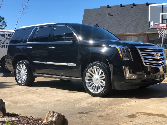 Black Cadillac Escalade parked on a sunny driveway beside a building