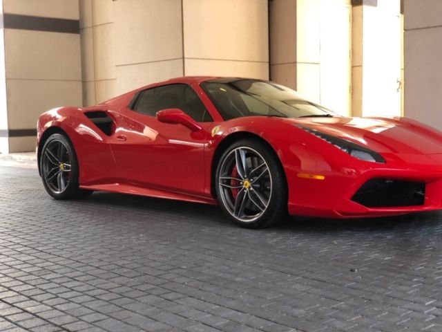 Red Ferrari sports car parked on a paved driveway beside beige columns