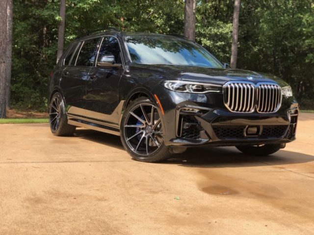 Black BMW SUV parked on a tan driveway with trees in the background