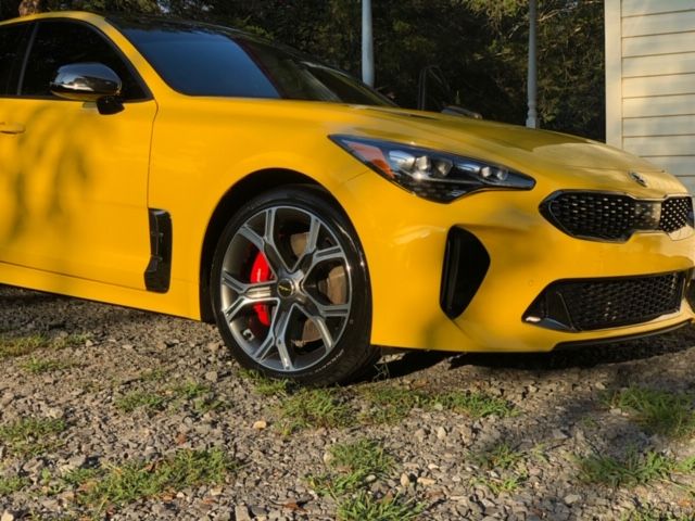 Yellow sports coupe parked on gravel beside a building, front side view with red brake calipers.