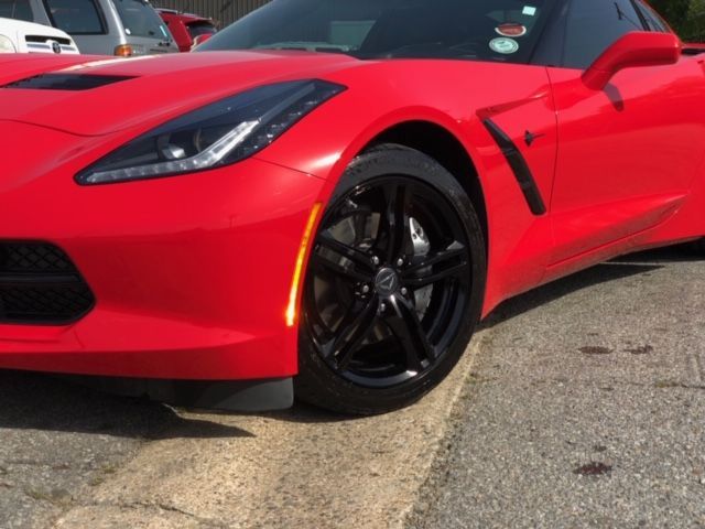 Red sports car parked on pavement, close-up of front side and wheel