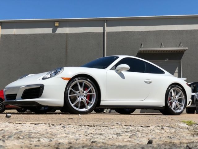 White sports car parked beside a gray building on a gravel surface