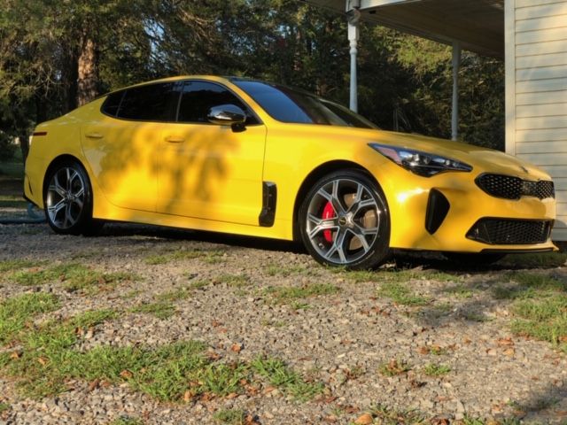 Yellow sports coupe parked on gravel beside a house, lit by late-afternoon sun.