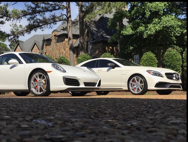 Two white sports cars parked side by side in front of a house with trees overhead