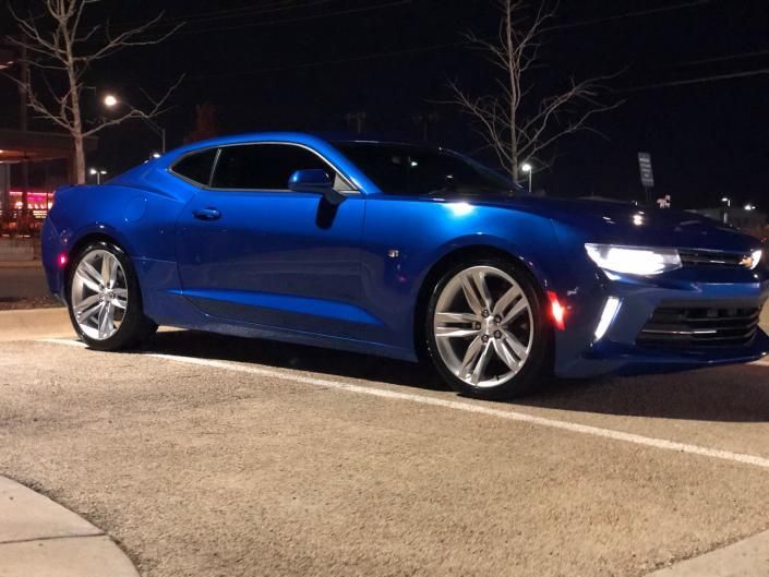 Blue sports coupe parked at night on a street, viewed from the side.