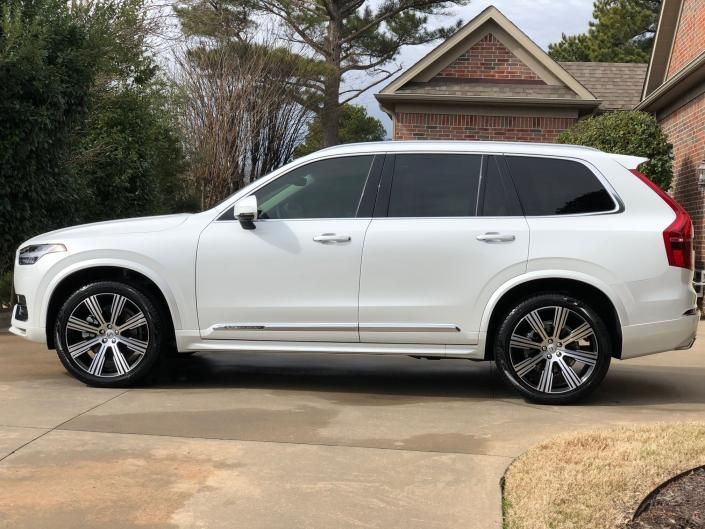 White SUV parked in a driveway beside a brick house, viewed from the side.