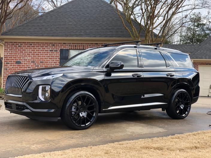 Black SUV parked in a driveway beside a brick house, with tinted windows and black rims.