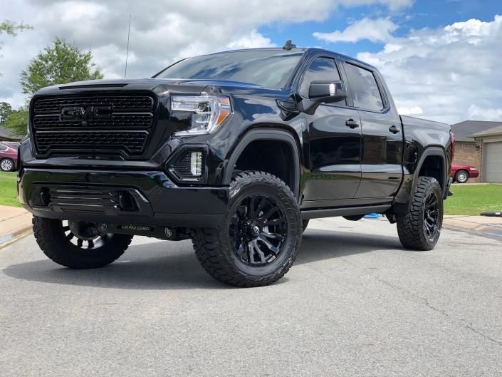Black lifted pickup truck parked on a street under a cloudy sky