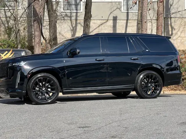 Black SUV parked on a street in front of leafless trees and a building.