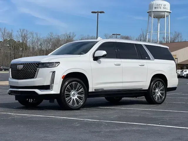 White Cadillac Escalade parked in a parking lot near a water tower on a clear day