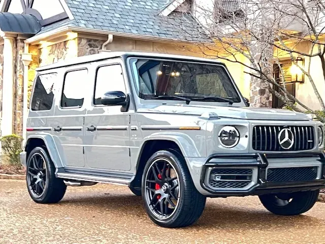 Silver Mercedes G-Class SUV parked in a driveway outside a house at dusk