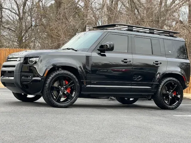 Black lifted SUV with roof rack and red brake calipers parked on a road, trees in background