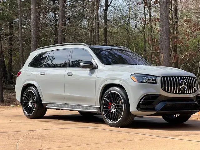 White SUV parked on a dirt road in a wooded area, side view with black wheels and tinted windows