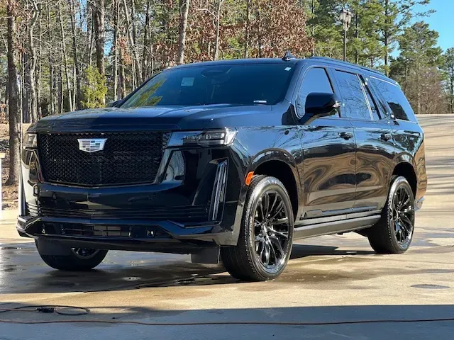 Black Cadillac SUV parked on a driveway with trees in the background