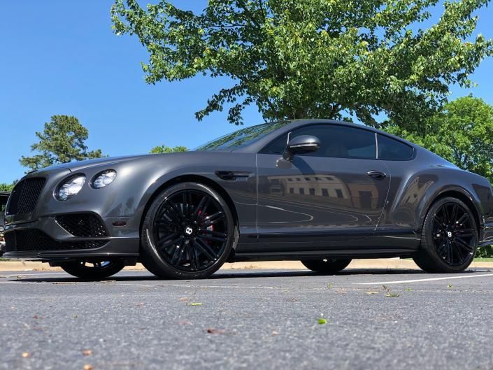 Dark gray luxury sports coupe parked on a street under green trees against a blue sky