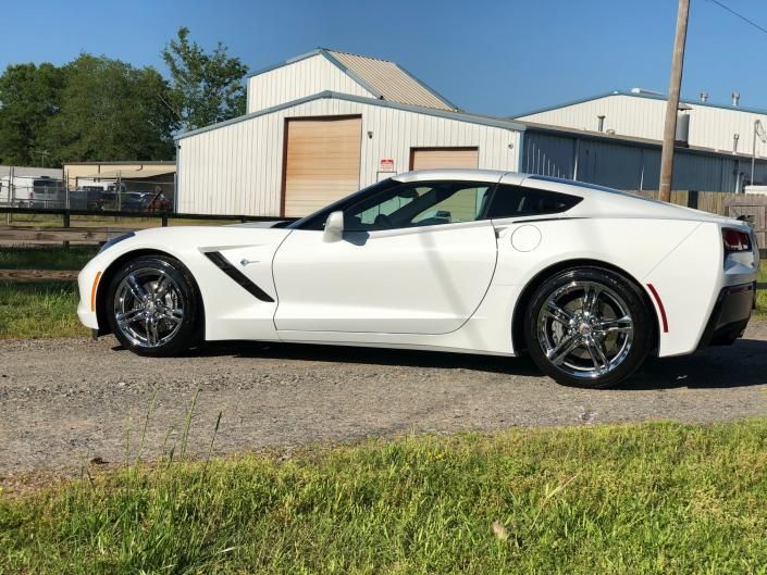 White sports car parked beside a garage on a sunny day