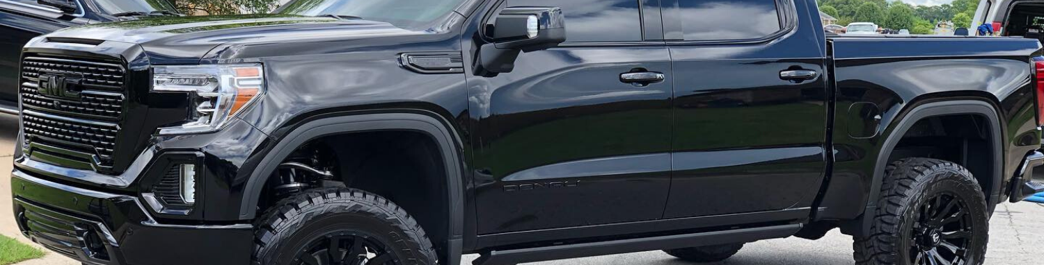 Black lifted pickup truck with large off-road tires parked outdoors in daylight
