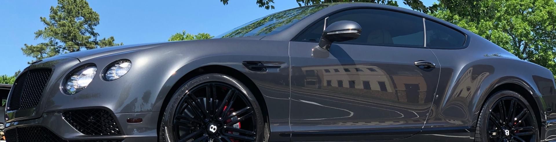 Gray sports coupe parked outdoors under a blue sky, side view with dark wheels and tinted windows
