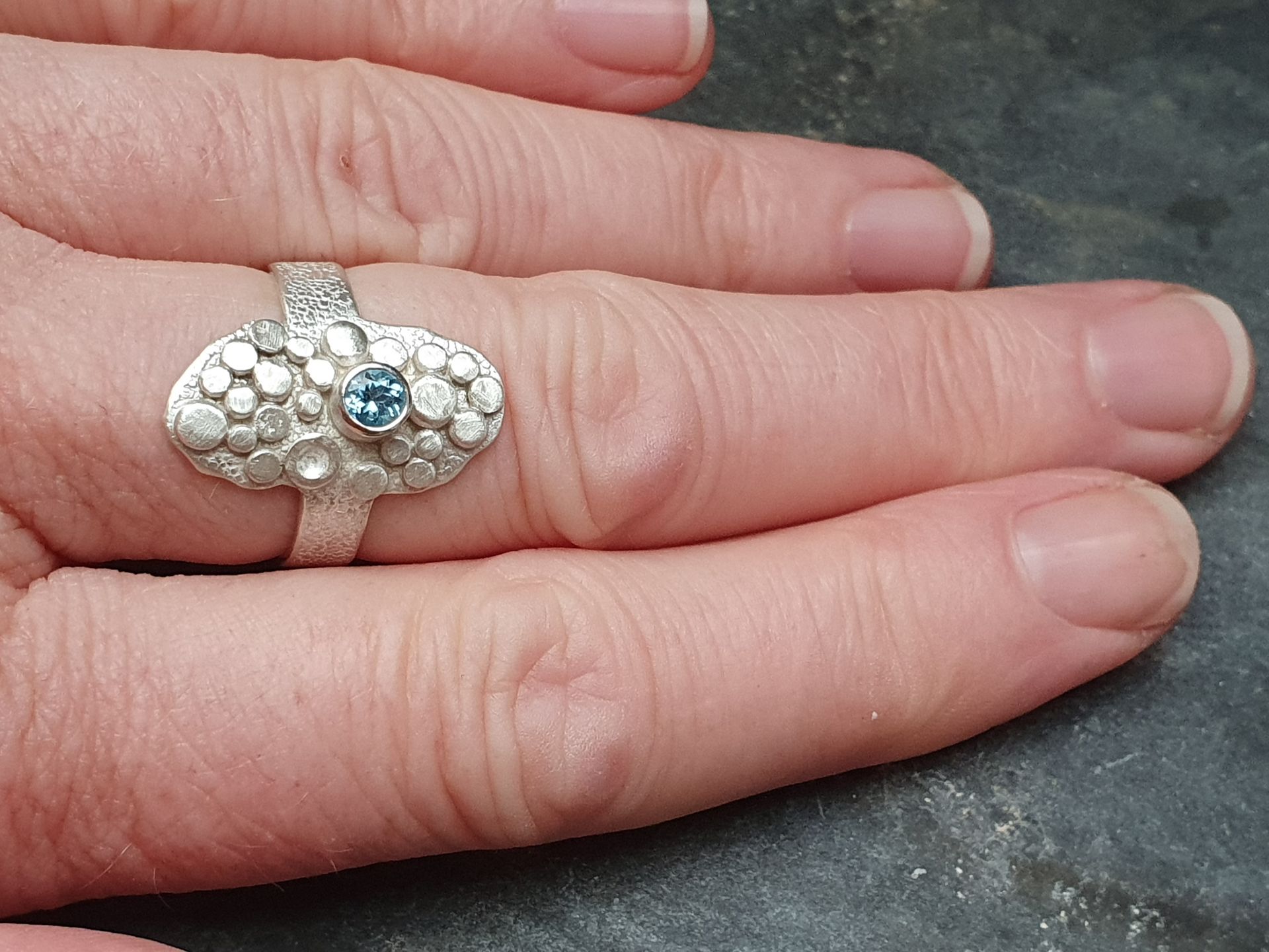 Zilveren ring met een gestructureerde band, ovale bovenkant met diverse verhoogde zilveren cirkels en een blauwe topaas.